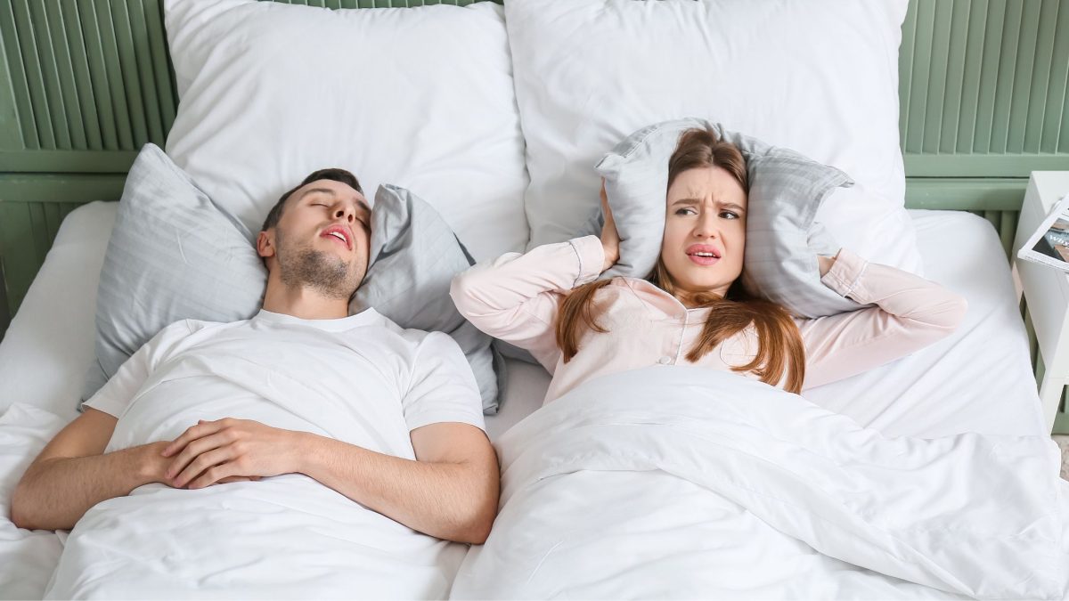 Husband snoring in bed, wife covering her ears with a pillow | SleepTest.co.uk